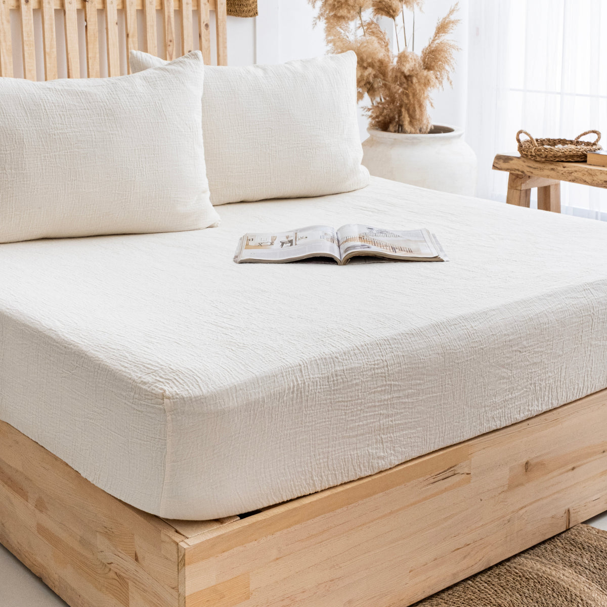 Ivory cotton muslin fitted sheet covering a mattress on a wooden bed