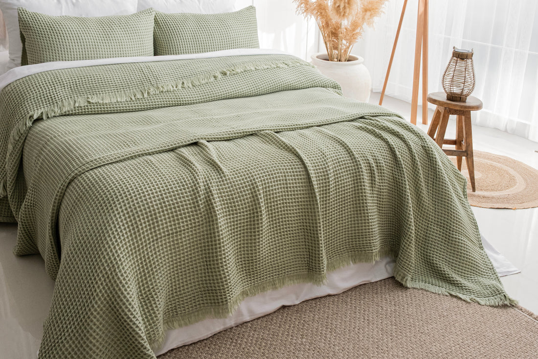 sage green organic cotton waffle blanket layered on a bed